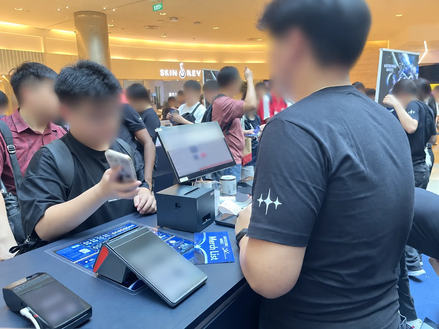 Customer and cashier at Rewardly POS checkout during online video games merchandise pop-up; faces and screens obscured