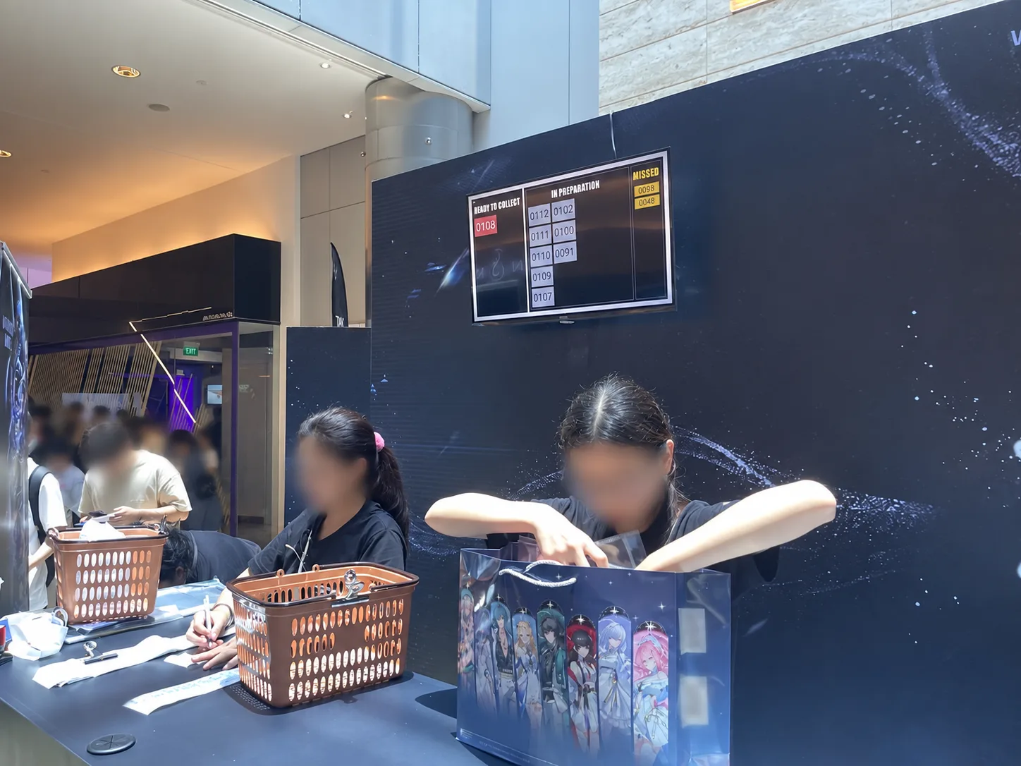 online video games merchandise packing station beneath an order collection queue display; faces obscured